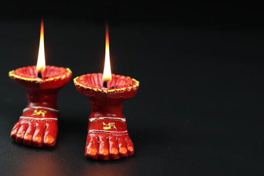 Clay Lamp Known As Diya, Deep, Diyo, Deepa Or Deepam WIth Goddess Feet Lakshmi Charan Illuminating In Dark Black Background With Copy Space For Text. Shubh Deepawali And Laxmi Pooja Theme