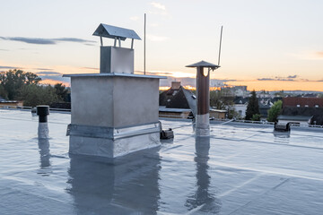 Flat roof covered with bitumen membrane and silver lacquer with chimney on a private house. Reflections after rain - obrazy, fototapety, plakaty