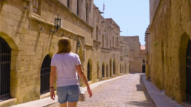 Slow motion female tourist sightseeing down old medieval cobblestone street of the knights in Rhodes, Greece 