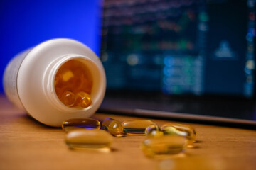 Omega 3 capsules on laptop at businessman workplace. Vitamins and supplements during stress at work.