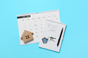 Calendar with pay rent mark, notepad, pen, key with keychain and figure of house on color background