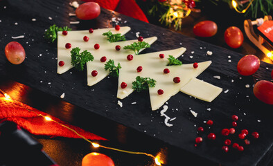 Creative Christmas tree made of cheese with herbs, spices, grapes and numbers 2022 on a cutting board.