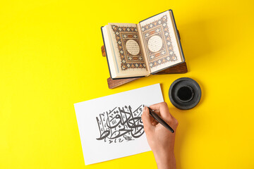 Arabic calligraphist writing on paper sheet against color background