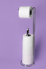 Holder with toilet paper rolls on purple background