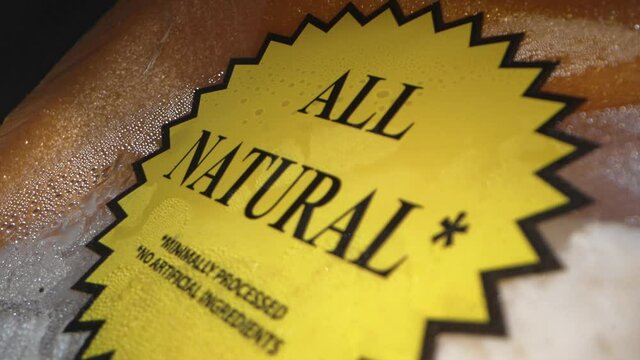 This macro, close up video shows a yellow "all natural" meat label on packaged chicken breast fading to unfocus.