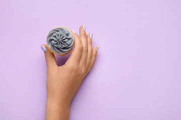 Woman with beautiful manicure holding cupcake on purple background