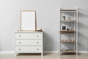 Blank poster frame on chest of drawers near light wall