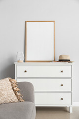 Modern chest of drawers with blank poster frame near light wall