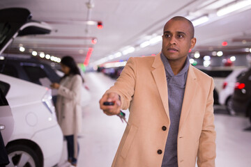 Elegant man opens car with car alarm keychain in underground parking