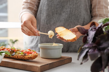 Woman spreading toast with dip at table in kitchen, closeup