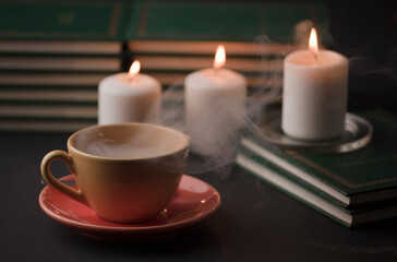 Obraz na płótnie Canvas cup of tea with hot smoke and lit candle. on the desk at home, power outage (focus on cup).