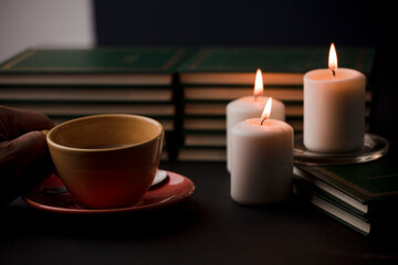 Fototapeta na wymiar cup of coffee with hot smoke and three burning candles. on the desk at home, power outage (focus on cup).