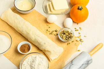 Raw dough and ingredients for preparing pumpkin strudel on light background