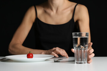Young woman at table on dark background. Anorexia concept