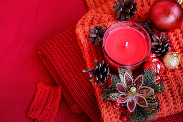 Christmas still life scene. Seasonal photo. Candle, pine cones, Christmas balls on knitted red background. Red color background.