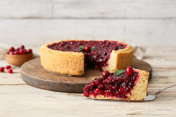 Spatula with piece of tasty lingonberry pie on light wooden table