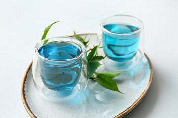 Obraz na płótnie Canvas Plate with glasses of blue tea on white background, closeup