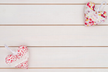 Two fabric heart pads pillows diagonally from each other on a white wooden background. 