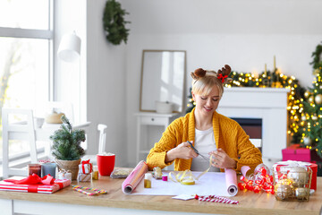 Beautiful young woman packing Christmas gift at home