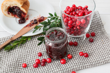 Jar with tasty lingonberry jam and fresh berries on white wooden background