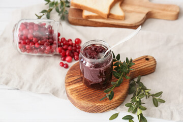 Jar with tasty lingonberry jam and fresh berries on white wooden background