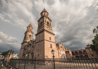 Fototapeta premium Morelia Cathedral, Michoacan, Mexico, at sunset, with rain clouds approaching. Church made of pink quarry like most of its buildings in the historic center.