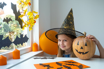 Smiling happy little girl in witch costume preparing for Halloween party at home. Holiday...