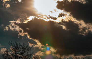 Landscape with a snow cloud and silhouettes of trees. Shooting against the sun. The rays of the sun have created colored reflections in the lens. Selective focus.