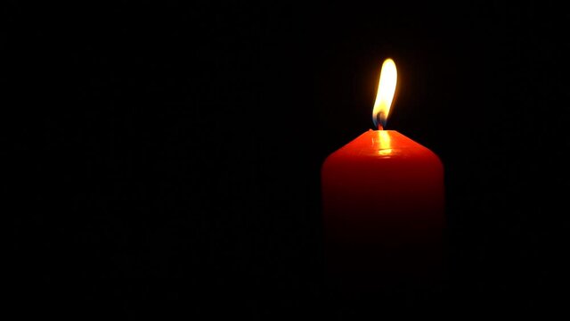 Single big red wax candle flame lights in the dark on a black background. Praying, hope and mourning concept.