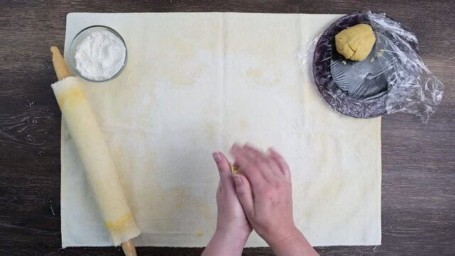 Woman’s hands kneading and shaping raw sugar dough in preparation for rolling it out, pastry cloth on a wood table
