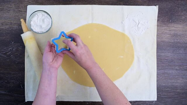 Woman’s hands cutting out star shape sugar cookies, pastry cloth on a wood table
