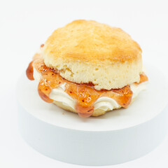Closeup of a fresh baked scone with fresh cream and raspberry jam.