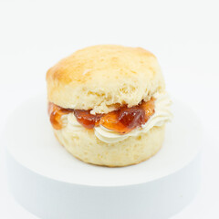 Closeup of a fresh baked scone with fresh cream and raspberry jam.