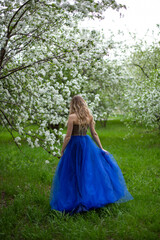 blonde girl in a blue dress in an apple orchard