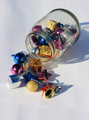 Christmas decorations are scattered from a glass jar on a white background. December.