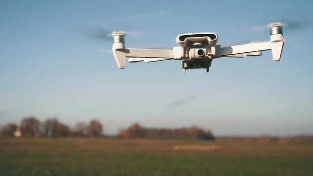 White Drone Flying on Nature Background. Drone Hanging in Air Flying Helicopter Dron Remote Control Air Drone. Slow Motion Shot.