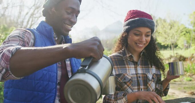 Smiling diverse couple drinking tea and hiking in countryside