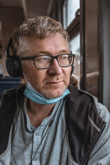 Portrait of an adult man wearing headphones and glasses with a medical protective mask on his chin...