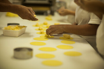 Human Hands making Raw and dry capeletti pasta on kitchen table