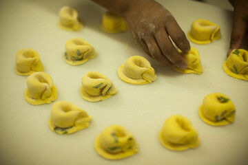 Human Hands making Raw and dry capeletti pasta on kitchen table