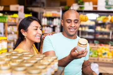Happy married couple choosing canned food at grocery store