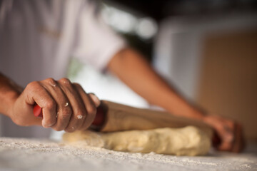 Obraz na płótnie Canvas Human Hand using dough rolling pin to make pasta - making Raw and dry pasta on kitchen table - flower