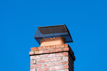 Chimney cap installed to prevent critters entry to home, attic, building. Brick chimney. Blue sky.
