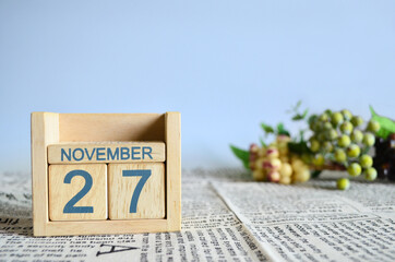 November 27, Calendar cover design with number cube with fruit on newspaper fabric and blue background.	
