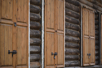 A wall of wooden logs with wooden shuttered windows closed with locks.