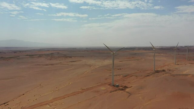 Panning Aerial drone shot of row of windmills in the desert with beautiful clouds