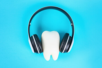 Tooth in white wireless headphones on a blue background. Teeth listening concept.