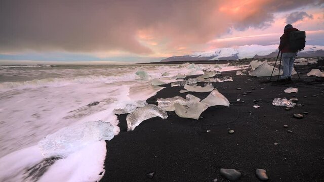 Professional Photographer taking pictures of famous Diamond Beach during sunrise in Iceland - Splashing waves flooding icebergs and ice cubes at black sandy beach