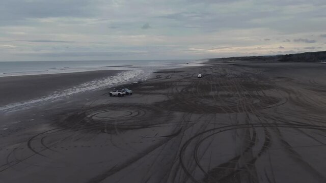 Aerial: Cars driving on the black sands of Muriwai Beach, Auckland, New Zealand