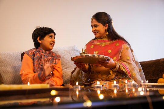 Indian woman sitting on sofa with holding a puja thali on her hand beside her son  during Diwali